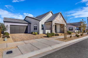 View of front of property with stone siding, driveway, an attached garage, and board and batten siding
