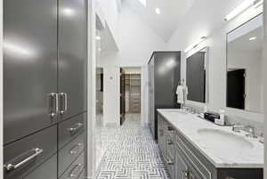 Full bathroom with double vanity, vaulted ceiling, a walk in closet, recessed lighting, and a skylight