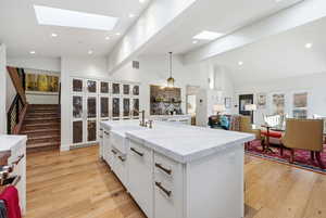 Kitchen featuring white cabinets, light stone counters, open floor plan, light wood-style flooring, and hanging light fixtures