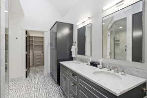Full bathroom with double vanity, a walk in closet, and a stall shower