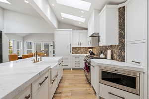 Kitchen featuring lofted ceiling, light stone counters, stainless steel appliances, light wood-type flooring, and backsplash