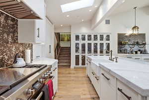 Kitchen featuring white cabinets, high end range, decorative backsplash, light stone counters, and pendant lighting
