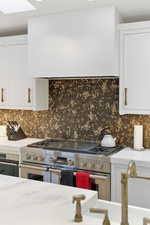 Kitchen with white cabinetry, double oven range, light stone counters, and range hood