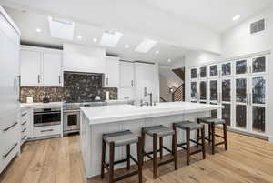 Kitchen featuring white cabinets, a breakfast bar, light stone counters, high end stainless steel range oven, and vaulted ceiling