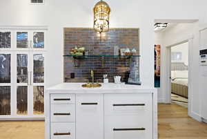 Bar area with white cabinetry, light wood-style flooring, light stone countertops, hanging light fixtures, and open shelves