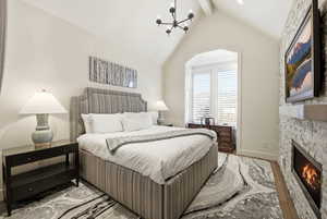 Bedroom with hanging lights, beam ceiling, a fireplace, and wood finished floors