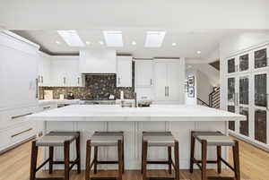 Kitchen featuring a center island with sink, a kitchen bar, white cabinets, light wood finished floors, and recessed lighting