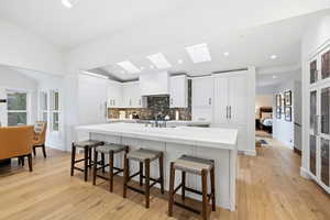 Kitchen with a breakfast bar area, white cabinets, a center island with sink, light wood-style flooring, and recessed lighting