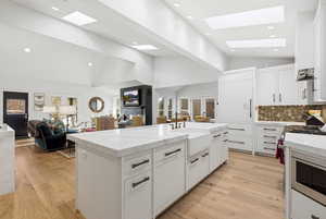 Kitchen featuring open floor plan, white cabinetry, light stone counters, a skylight, and lofted ceiling