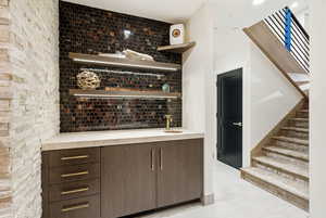 Bar featuring open shelves, decorative backsplash, modern cabinets, and dark wood finish cabinets