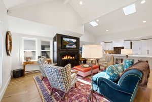 Living area featuring wood finished floors, a lit fireplace, vaulted ceiling, a skylight, and recessed lighting