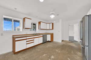 Kitchen featuring brown cabinetry, white cabinets, appliances with stainless steel finishes, unfinished concrete floors, and light countertops