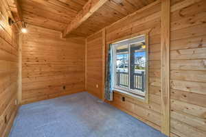 Carpeted empty room featuring a wood ceiling with exposed beams and wooden walls