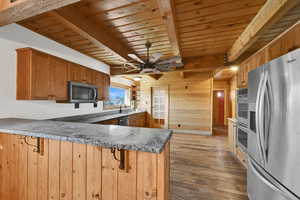 Kitchen with wood walls, appliances with stainless steel finishes, a peninsula, a wood ceiling with exposed beams, and light wood-style floors