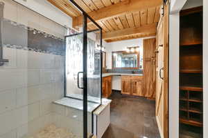 Full bath with vanity, a stall shower, a wood ceiling with exposed beams, and dark stone finish floors