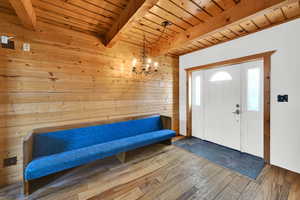 Entrance foyer with hardwood / wood-style flooring, wood walls, a wood ceiling with exposed beams, and a chandelier