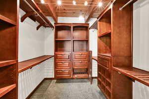 Walk in closet with dark carpet and beamed ceiling