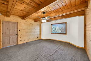 Unfurnished room featuring wooden walls, carpet, a wood ceiling with exposed beams, and ceiling fan