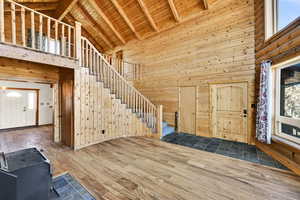 Entrance foyer featuring high vaulted ceiling, stairs, hardwood / wood-style flooring, a wood ceiling with exposed beams, and wood walls