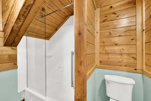 Bathroom featuring wood ceiling, shower / bathtub combination, lofted ceiling, and wooden walls