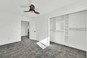 Unfurnished bedroom with dark carpet, a ceiling fan, and a closet