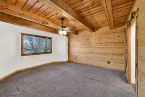 Carpeted empty room with wood walls, a wooden ceiling with exposed beams, and ceiling fan