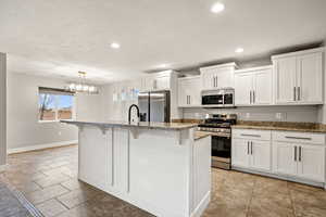 Kitchen with light stone counters, stainless steel appliances, a breakfast bar area, white cabinetry, and a textured ceiling