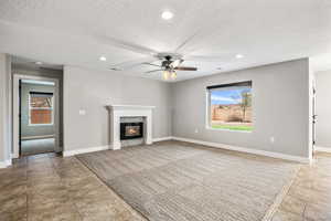Unfurnished living room with recessed lighting, ceiling fan, a glass covered fireplace, light tile patterned floors, and a textured ceiling