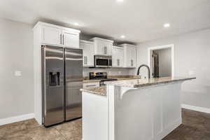 Kitchen with stainless steel appliances, light stone countertops, white cabinetry, a breakfast bar area, and recessed lighting