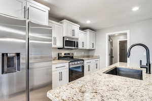 Kitchen with stainless steel appliances, light stone countertops, white cabinets, and recessed lighting