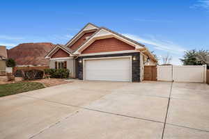 View of front of home with a gate, driveway, stone siding, an attached garage, and a mountain view