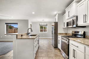 Kitchen featuring stainless steel appliances, white cabinets, a center island with sink, light stone counters, and a textured ceiling