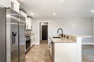 Kitchen with stainless steel appliances, light stone countertops, white cabinets, a center island with sink, and recessed lighting