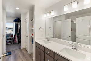 Bathroom featuring double vanity, a spacious closet, light wood finished floors, and recessed lighting