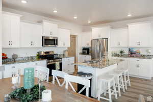Kitchen with stainless steel appliances, light stone countertops, white cabinets, a breakfast bar, and an island with sink