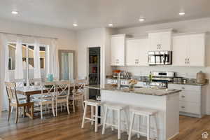 Kitchen featuring stainless steel appliances, white cabinets, light stone counters, dark wood-style floors, and a kitchen bar
