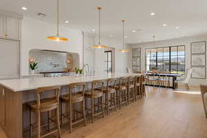 Dual tone kitchen featuring tasteful backsplash, a large island, light wood-type flooring, light stone counters, and a breakfast bar area