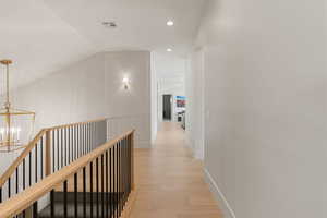 Hall with light wood-type flooring, a decorative wall, vaulted ceiling, and suspended lighting