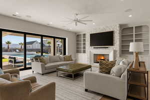 Living room featuring built in shelves, a fireplace, a ceiling fan, wood finished floors, and recessed lighting