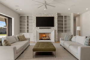 Living room featuring built in shelves, a warm lit fireplace, ceiling fan, recessed lighting, and wood finished floors
