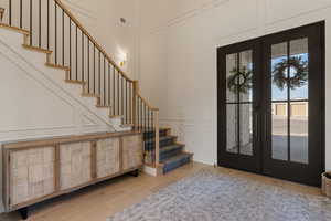 Foyer entrance featuring a decorative wall, french doors, light wood-type flooring, and a high ceiling