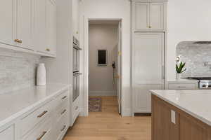 Kitchen with backsplash, light stone counters, light wood-type flooring, two tone color scheme, and stainless steel double oven