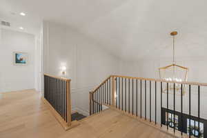 Hall featuring lofted ceiling, light wood-style floors, a decorative wall, an upstairs landing, and suspended lighting