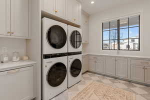 Laundry area with stacked washer and clothes dryer, recessed lighting, and cabinet space