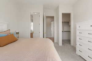 Bedroom featuring a spacious closet, light carpet, and ensuite bath