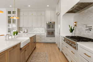 Kitchen featuring dual tone cabinetry, stainless steel appliances, light wood-style flooring, hanging light fixtures, and light stone countertops
