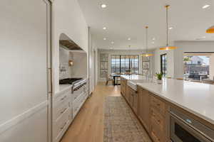Kitchen featuring dual tone cabinetry, decorative light fixtures, light wood finished floors, light stone countertops, and stainless steel appliances