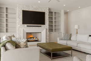 Living room with built in shelves, a stone fireplace, recessed lighting, and ceiling fan
