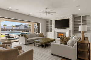 Living area featuring built in shelves, a fireplace, ceiling fan, and recessed lighting