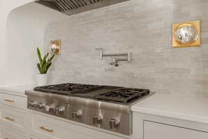 Kitchen view of stainless steel gas stovetop, backsplash, light stone countertops, and white cabinets